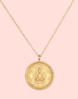 The Gold Buddha Pendant Necklace features a round pendant engraved with a seated Buddha at the center, framed by a decorative border. Finished in 18kt gold plate, it hangs from a delicate chain for an elegant look.