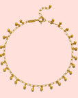 The Joyful Anklet is a delicate 18k gold plated anklet with small dangling gold beads spaced along a fine oval cable chain, finished with an adjustable clasp.