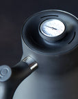 A close-up of the Stagg Pour-Over Kettle (Stovetop), a black kettle with a precision spout and built-in brew-range thermometer on the lid displaying the Fellow brand, set against a dark background.