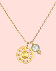 The Blue Topaz Sun Pendant Necklace features a gold-plated sun-shaped pendant with a textured center and dotted rays, paired with a small round blue topaz charm accented by three tiny gold beads for radiant style.