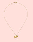 The Blue Topaz Sun Pendant Necklace features a delicate gold plated chain with a round, textured gold pendant and a small blue topaz gemstone charm, displayed on a white background.