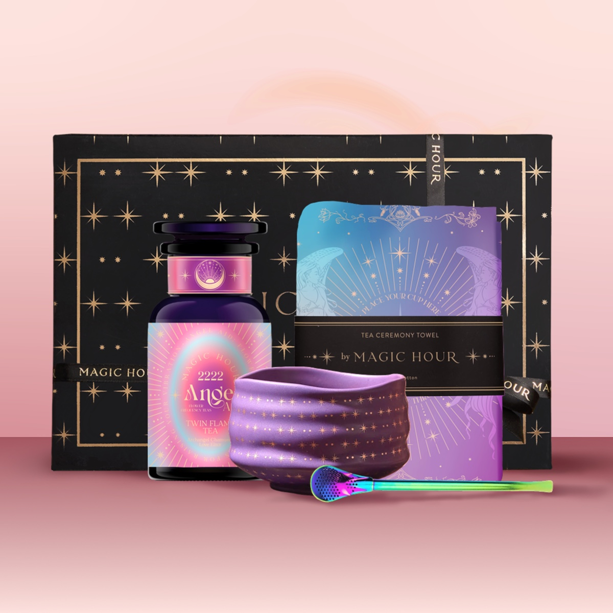 The Angel Numerology Fruit & Flower Tea Gift Set includes a black and gold box, "Angel 2222" bottle, celestial tea towel, purple starry bowl, and green-handled spoon—artfully displayed on a pink gradient background.