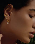 A woman with smooth skin wears the Freedom to Soar Butterfly Stud Earrings, a small crystal stud, and a gold hoop with a dangling pearl, gazing downward serenely against a softly blurred background.