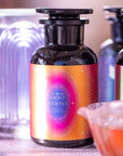 A close-up of a dark glass bottle with a vibrant "555" label, reading "Journey" and "You Are On the Right Path," is surrounded by softly blurred bottles. The background has a warm glow and a partially visible glass dish.