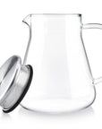The Teabloom One-touch Tea Maker (15 oz/1-2 cups) features a clear glass carafe with handle and a round silver metal lid with built-in mesh strainer, showcased empty in a minimalist style against a white background.