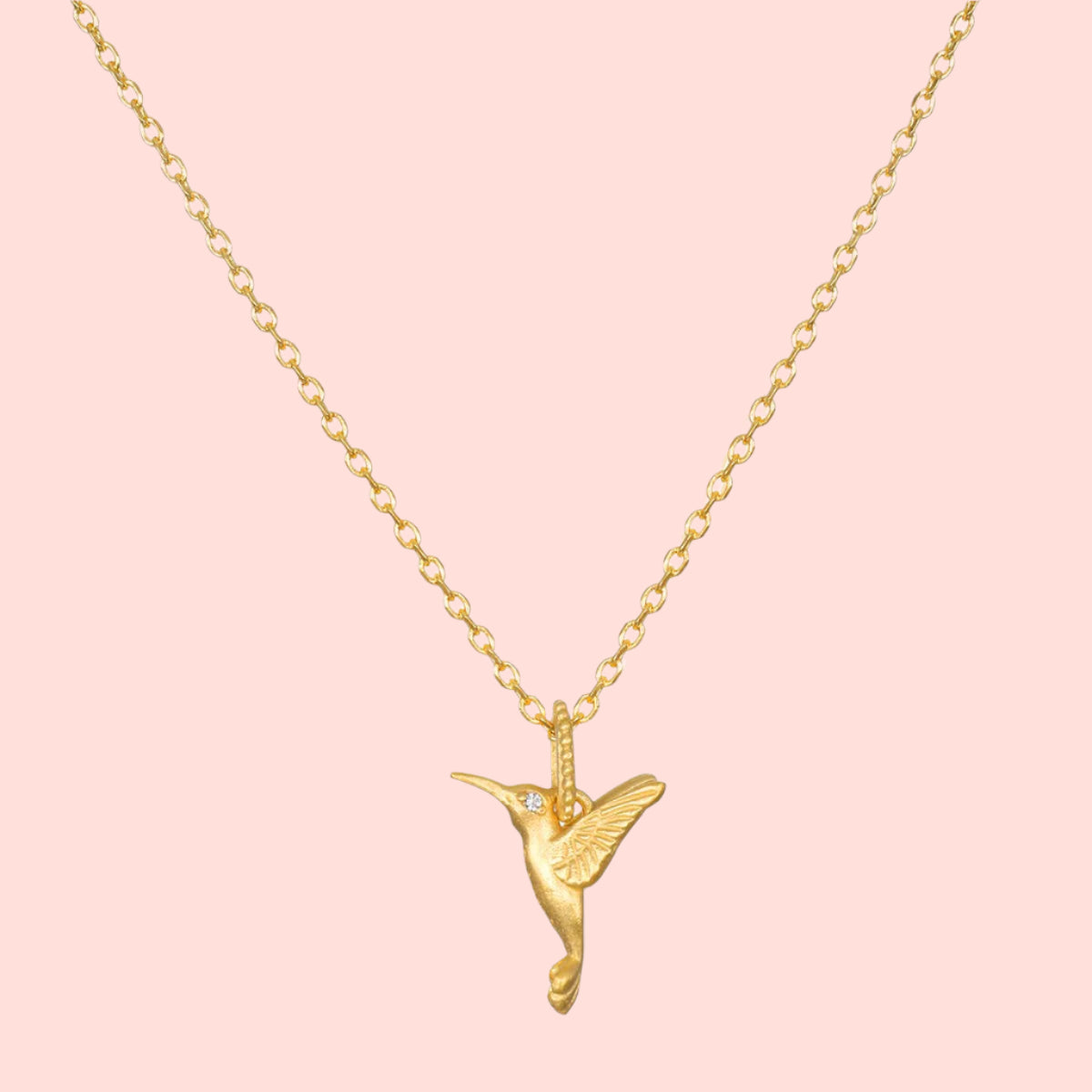 The Loving Devotion Hummingbird Necklace 16" features a detailed pendant on a gold chain, highlighted by a sparkling white topaz accent for the bird's eye and finished in 18k gold plating.