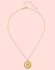 The 18" Sunburst Medallion Necklace features a gold plated, thin beaded chain and a round, textured sun-moon-star pendant with a central gemstone, shown on a plain white background.