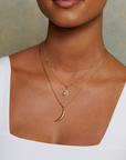 A woman wearing a white square-neck top and two gold necklaces: one is the 16" Labradorite North Star Necklace layered with a sun pendant. Only her neck and shoulders are visible.
