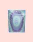 A pastel, holographic pouch labeled "999: Divine Completion" features radiating lines, star designs, and celestial-themed graphics, evoking spiritual completion against a light pink background.