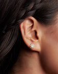 A close-up of a woman with braided dark hair wearing Blue Topaz Starburst Earrings—sun-shaped studs with blue topaz centers set in 18k gold plate.