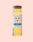 A tall glass jar with a brown lid holds light golden, single-varietal raw Acacia honey. The label says "Savannah Bee Co. Honey - Acacia, Pure & Natural," and features a bee on a soft pink background. It's truly premium, Net Wt. 12 oz (340 g).