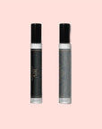 Two Air Essential Oil Perfume roller bottles with black caps rest on a light pink background. The left bottle features a dark label with gold stars; the right one has a grey label adorned with geometric gold patterns.