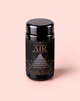 A black cylindrical tea canister labeled “Air: Mint, Mullein & Citrus Tea for Respiratory Support” sits on a light pink background. The label showcases gold geometric designs and text highlighting mental clarity, respiratory wellness, and a refreshing rosemary spearmint flavor—all thoughtfully crafted with decaf green tea.