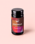A jar of Fireside Chai: Warming Rooibos Blend for Creating Connection, a caffeine-free spiced herbal dessert tea by Magic Hour, features a black lid and warm-toned labels with the words “Sip Curiously” on a soft pink background. This antioxidant-rich rooibos blend invites cozy moments with every cup.