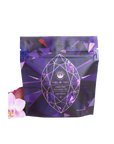 A purple and blue geometric patterned package of "Rest, Relaxation & Sleep Sampler Set" labeled "Amethyst." The packaging features a large, faceted gemstone graphic. An orchid flower is partially visible at the bottom left. This organic loose leaf tea weighs 4 oz.