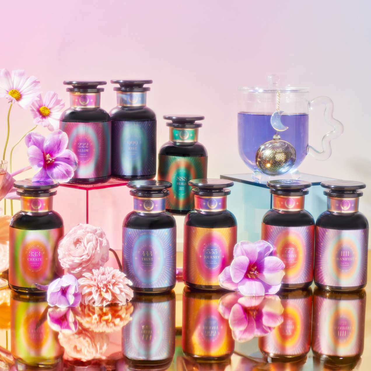Eight iridescent perfume bottles, pastel flowers, a glass teacup of blue Angel Tea, and a gold tea infuser are displayed on mirrored platforms with a pastel gradient backdrop for the Angel Tea Journey Subscription.