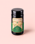Apple Almond Nog black tea tin, adorned with an elegant green and gold label, sits against a light pink background. This festive eggnog-inspired blend combines rich black tea with organic almonds for a comforting holiday sip.