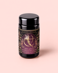 A black tea canister labeled “Artemis of the Wilds: Wild Moon White Tea” features a gold-illustrated woman with a bow and arrow, surrounded by floral designs and delicate butterfly pea flower accents on a mauve background.
