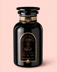 A black glass jar labeled “Bliss: Sacred Tulsi Adaptogen Tea” with gold accents, adorned with an illustration of pouring liquid and the phrases “Time for Infinity” and “Magic Hour,” sits atop a pale pink background—evoking the calming properties of Holy Basil, traditionally used to soothe the nervous system.