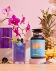 A vibrant scene featuring Blue Pineapple: Ceremonial Soda Pop Tea—an antioxidant-rich purple drink with Butterfly Pea Flower, served in a glass and pitcher, surrounded by orchids, pineapple, and yellow flowers.