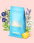 A blue bag of Blue Pineapple: Ceremonial Soda Pop Tea, labeled "Blue Pineapple," sits on a pale pink background surrounded by flowers and a pineapple wedge. This caffeine-free herbal blend features vibrant Blue Spirulina and Butterfly Pea Flower, and the bag is printed with the message, "The Future is Full Leaf.