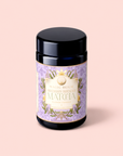 A dark jar with a lavender and gold label reading "Flower Powder: Blueberry Lavender Matcha" sits on a pale pink background, evoking the soothing essence of blueberry matcha and calming aromatherapy.