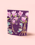 The "Breakfast in Paris-Oolong Black Tea Scented with Fruits & Flowers of Secret Parisian Gardens" comes in a purple package adorned with magnolia flowers, teacups, teapots, and a golden Eiffel Tower on a pale pink background.