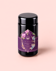 A black tea canister adorned with a purple and floral geometric label reading “Breakfast in Paris-Oolong Black Tea Scented with Fruits & Flowers of Secret Parisian Gardens,” set against a pale pink backdrop—this romantic blend encapsulates the essence of an authentic Parisian black tea experience.