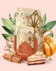 A decorative bag of Pumpkin Spice Cake Batter Breakfast tea—an organic black tea and gut-healthy Puerh pumpkin spice breakfast blend—is surrounded by a pumpkin, cinnamon sticks, ginger root, green leaves, and a slice of layered cake, all set against a pale pink background.