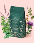 A dark green "Divine Timing Calm" package with gold botanical designs is surrounded by colorful illustrated herbs and flowers, highlighting its cooling mint adaptogen blend on a light pink background.