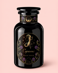 A black glass bottle labeled “Capricorn: Maple Oolong Tea” features a gold and purple zodiac-themed Capricorn design with floral details and “Magic Hour” text, emphasizing the metabolism-boosting benefits of Ti Quan Yin Oolong and Se Chung Oolong, all set against a soft pink background.
