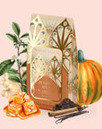 A charming bag of Pumpkin Spice Caramel Oolong is nestled among a pumpkin, aromatic spices, caramel squares, vanilla beans, ginger, and seasonal leaves—all set against a soft pink backdrop—capturing the inviting scent of an autumn harvest blend. This cozy pumpkin caramel oolong tea is an ideal companion for relaxing moments and provides a flavorful way to enjoy metabolism-supporting tea all season long.