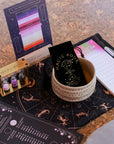 The Tea Ceremony Starter Set includes a zodiac mat, 2025 moon phase calendar, astrology tea towel, notepad, vials in a holder, chart, and a ceremonial black bowl with a "Magic Hour" card—perfect for astrology enthusiasts.
