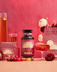 A vibrant pink-themed display shows Cherry Cola Black Tea: Ceremonial Soda Pop Tea with Sugar "Destroyer," served in a glass with a floral garnish, alongside its packaging, a tall carafe, pomegranate, and fresh flowers on the table.