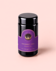 A black jar with a purple label reading “Zhena’s Original Coconut Chai” sits on a pale pink background. Crafted with organic spices, this coconut chai blend promises a deliciously aromatic experience. The label also shows the net weight as 1oz/28g.