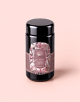 A black jar with a geometric pink and silver label stands upright on a pale pink background. The label features diamond shapes and text, highlighting “Diamond - Champagne & Strawberry Jasmine White Tea for Beautiful Skin,” suggesting this is a luxurious, high-end infusion crafted to promote beautiful skin.