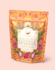 A vibrant pouch labeled "Flower Powder: Dragon Fruit Matcha," adorned with floral patterns, dragon fruit artwork, and a gold-highlighted label on a peach background, captures the lively essence of this blend, which combines juicy dragon fruit with premium ceremonial matcha to support gut health.
