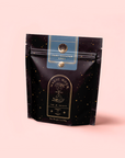 A black resealable pouch labeled "Earl Greater Grey: Tea for the Bright & Bold" contains organic Earl Grey tea, with gold stars and a celestial design on a light pink background.