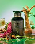 A dark green bottle labeled "Earth: Stabilizing and Nourishing Herbs, Roots, and Puerh tea" sits with flowers, bark, moss, a glass teacup of grounding tea, and a branch on a glossy surface against a green background for immune support.