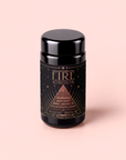 A black jar labeled “Fire: Spiced Black Tea with Ginger and Cardamom to Ignite Courage and Vitality” by Magic Hour, featuring gold stars and text, sits on a light pink background. This Fire Tea is expertly crafted with spiced black tea, ginger, and cardamom to ignite courage and vitality for a revitalizing experience.