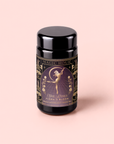 A beautifully designed black tea canister labeled “Magic Hour” features a dancing woman with flowers, gold accents, and the text “Flora In Bloom: Peach Moonlight White Tea, The Pisces” on a light pink background. This elegant canister celebrates the delicate essence of Yue Guang Bai—also known as Moonlight White Tea—one of the most enchanting white teas.
