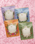 The Flower Powder: Matcha Bundle features four vibrant tea pouches, like Strawberry Matcha and Blueberry Lavender Matcha, arranged in floral packaging with a pink illustrated background for a whimsical botanical look.