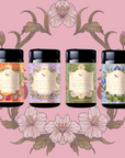 Four colorful Flower Powder: Matcha Bundle canisters with floral labels are displayed side by side on a pink background with illustrated flowers and leaves. Each features a unique matcha flavor, such as Strawberry Matcha and Blueberry Lavender Matcha.