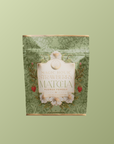 A decorative green pouch labeled "Flower Powder: Strawberry Matcha," with floral and strawberry illustrations, showcases organic ceremonial matcha on a solid light green background.