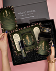 A person opens a black “MAGIC HOUR” gift box containing the Monthly Magic Tea Journey Subscription: goddess tea, a ritual guide, spray bottle, and tea description card with floral and celestial designs on a pink background.