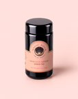 A black cylindrical tin labeled “Goddess Green Tea,” embellished with a peach and gold label, rests on a light peach background. This exquisite blend offers notes of apricot lychee and gentle lemongrass, elevating the classic green tea experience.