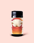 A cylindrical container of Magic Hour's "Tea for Energy: Bohemian Breakfast: Rich Puerh Black Tea Blend," featuring a sunburst design, pink and gold accents, and floral details, is set against a pale pink background—this organic puerh tea blend is known to support energy and digestion.