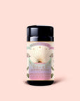 A container of Tea for Joy: Almond Matcha: Green Matcha Tea with Almonds, an antioxidant-rich matcha blend featuring a sunburst design label, set against a light pink background.