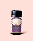 A jar of Tea for Harmony: Queen of Wellness: Women's Cycle Herbal Blend, adorned with a purple and gold label featuring botanical artwork and a sunburst design, set against a light pink background. This women’s herbal tea blends the nurturing qualities of organic chaste berry and calming raspberry leaf tea to help support balance throughout your cycle.