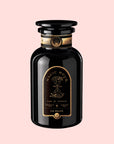 A black glass bottle with a gold and black label reading “Magic Hour” and “Time for Infinity,” featuring an hourglass illustration and the product name “Sin Eraser™ : Puerh Tea,” evokes the rich tradition of vintage Puerh. This striking piece stands out on a light pink background, blending timeless elegance with the essence of fine Puerh tea.
